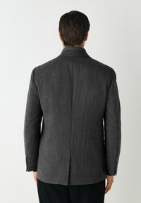 Blazer grigio a spina di pesce con una vestibilità strutturata, apertura posteriore singola e rever a punta. Presenta polsini con bottone e silhouette sagomata.