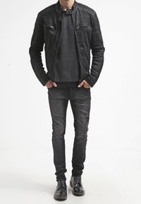 Veste en cuir noire avec détails texturés aux épaules et aux bras, associée à un pull à pois noir et blanc, un jean noir slim et des chaussures noires.