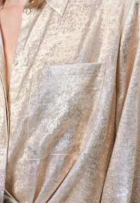 Metallic beige button-up shirt with a shiny texture, featuring a chest pocket and a classic collar design.