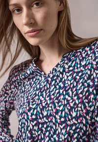 Blusa multicolore con una base blu navy e motivi astratti in rosa, blu e bianco, e design con colletto a scollo a pattina. Tessuto dalla consistenza liscia.