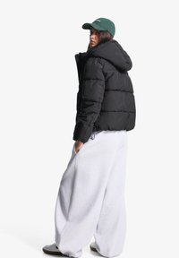 Giubbotto puffer nero con cappuccio, caratterizzato da un design trapuntato e tasche laterali, abbinato a pantaloni della tuta grigi oversize e sneakers bianche.