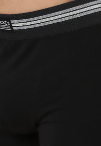 Boxer briefs pretas com uma cintura elástica e suave, apresentando duas riscas brancas. O tecido parece liso e elástico, garantindo conforto.
