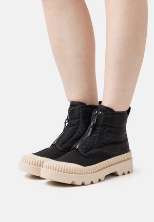 Black ankle boots with quilted fabric and front zipper. Thick cream rubber sole with ribbed edges. Smooth texture, modern design.