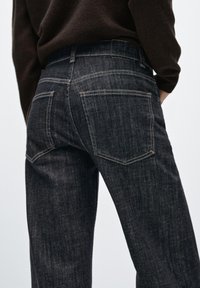 Mörka jeans i denim med rak skärning, utrustade med två bakfickor och kontrastsömmar. Tyget verkar robust med en subtil textur.