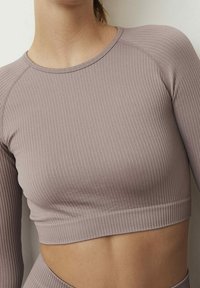 Pyłowy, jasny fioletowy top na ramiączkach z prążkowanej dzianiny, z długimi rękawami, zaokrąglonym dekoltem i wycięciem na wysokości talii dla dodatkowej wentylacji.