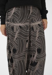 Pantalon large en tissu noir avec un motif de vagues crème. Taille élastique et texture douce. Gros plan détaillé du design.
