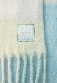 Könnyű gyapjú takaró pasztell zöld és kék árnyalatokban, puha rojtos szélekkel és varrt Calvin Klein címkével.