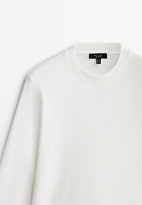 Hvid langærmet sweatshirt med ribbet rund hals. Fremstillet af blødt stof, med et minimalistisk design og et mærke ved halsen.