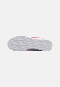 White sneaker sole with herringbone pattern, featuring a prominent Nike logo, red accents along the edge, and a smooth textured surface.