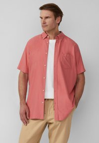 Korte mouwen, button-up overhemd in koraalkleurige stof, met een patch pocket, kraaghals, en gedragen over een wit t-shirt, gecombineerd met beige broek.