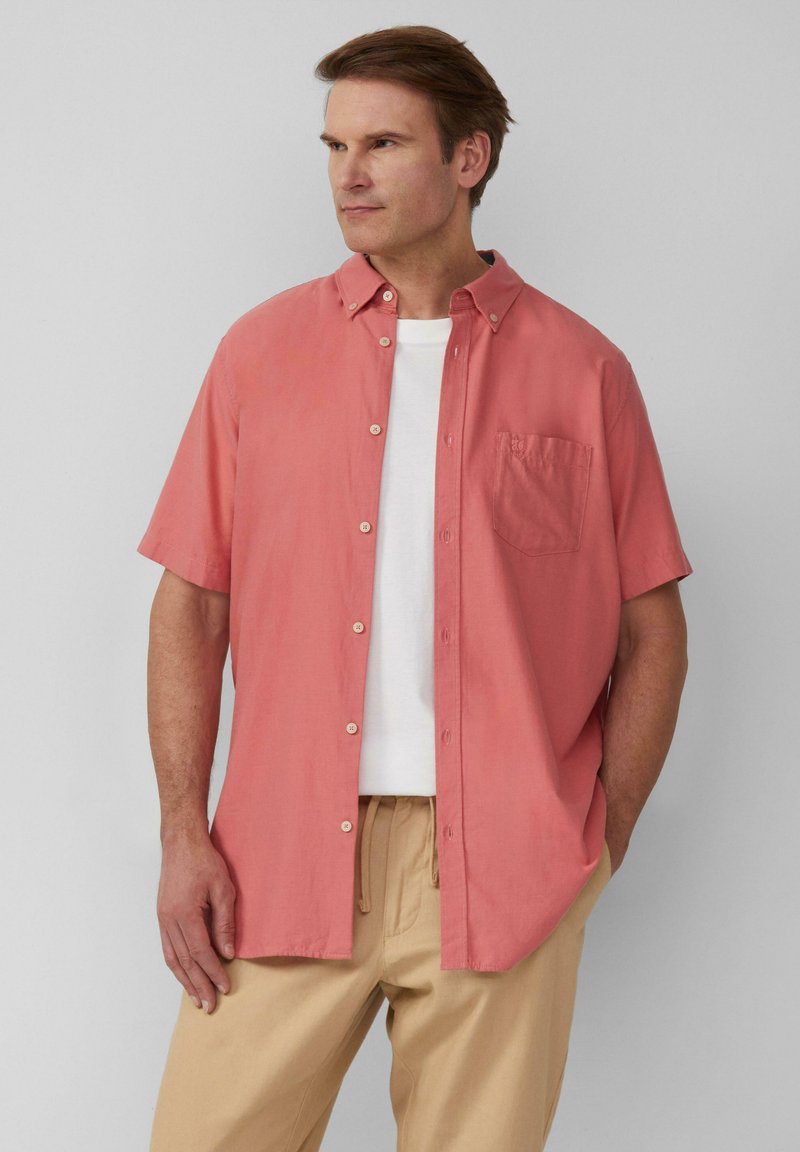 Korte mouwen, button-up overhemd in koraalkleurige stof, met een patch pocket, kraaghals, en gedragen over een wit t-shirt, gecombineerd met beige broek.