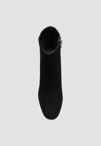Bottine en daim noir avec un bout pointu, un design épuré et un détail de fermeture éclair sur le côté. Texture lisse avec une silhouette ajustée.