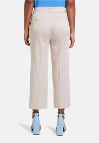 Licht-beige wijde broek met een soepele textuur en riemlussen, voorzien van twee subtiele achterzakken. Gecombineerd met blauwe blokhakken.