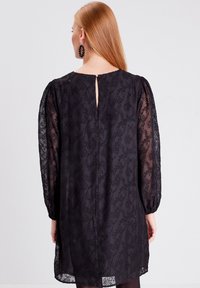 Black dress made of sheer fabric with a floral pattern, long puff sleeves, and a back keyhole detail. Subtle texture and lightweight design.