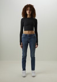 Top court à manches longues noir associé à un jean en denim bleu. La tenue présente un design ajusté avec une légère extensibilité et un style classique à cinq poches.