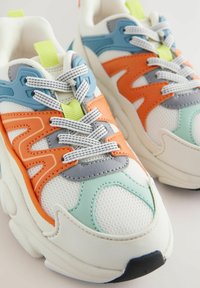 Igrzyskowe białe sneakersy z siateczkowych i skórzanych materiałów. Posiadają niebieskie, pomarańczowe, szare i miętowe akcenty, teksturowaną podeszwę oraz dekoracyjne sznurowanie.