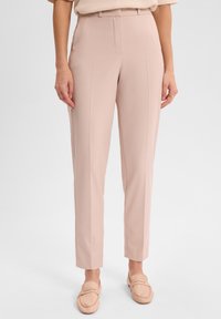 Jasnoróżowe spodni dostosowane, o gładkiej teksturze, prostej nogawce i szwach bocznych. W połączeniu z beżowymi butami wsuwanymi.