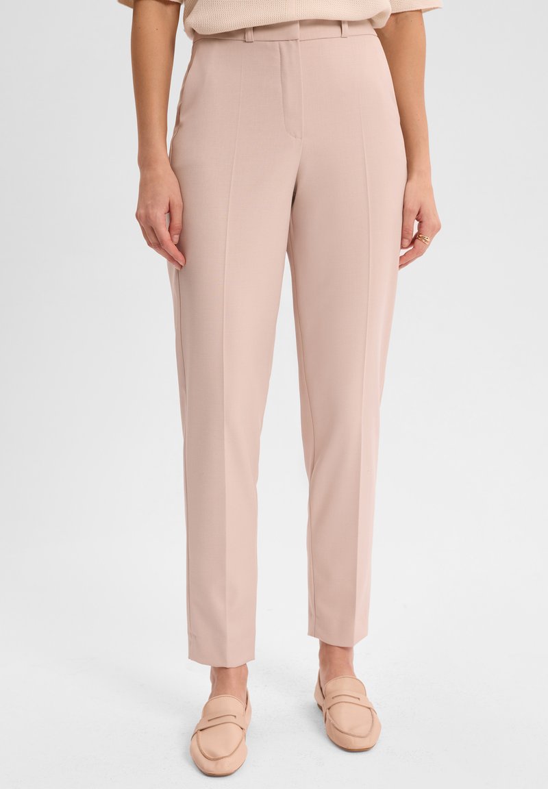 Jasnoróżowe spodni dostosowane, o gładkiej teksturze, prostej nogawce i szwach bocznych. W połączeniu z beżowymi butami wsuwanymi.