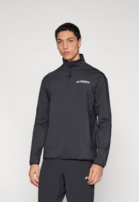 Melns Terrex zip-up džemperis ar garām piedurknēm, viegls materiāls, apkakle un balts logotips uz krūtīm. Gluda tekstūra.