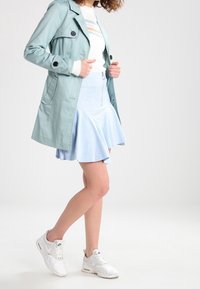 Vaaleansininen trench-takki, valkoinen teksturoitu neule, leveälahkeinen pastellisävyinen hame ja valkoiset tennarit. Pehmeä, sileä kangas, joka yhdistää erilaisia tyylejä.