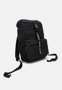 Zaino nero con design a roll-top, spallacci regolabili, tasca frontale con zip e pannello laterale in rete. Presenta un dettaglio del logo sulla tracolla.