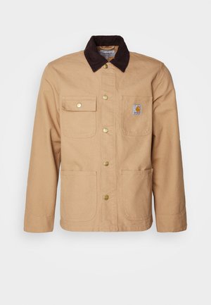 Beige Arbeitsjacke aus robustem Material, mit einem dunkelbraunen Cordkragen, Knopfleiste und vier Fronttaschen mit goldenen Knöpfen.