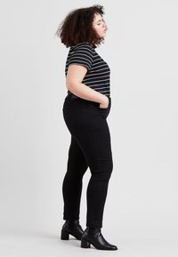 Svarte skinny jeans kombinert med en stripete svart og hvit t-skjorte. Modellen står på siden, iført svarte ankelstøvler med blokkhæl.