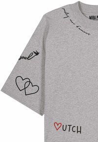 Chemise grise manches courtes avec écriture noire, deux cœurs noirs en contour sur la manche, un cœur rouge remplaçant le "D" du mot "Dutch" sur le devant.