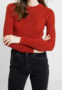 Rode geribbelde longsleeve top met een ronde halslijn, gecombineerd met hoge taille zwarte jeans. De stof lijkt zacht en aansluitend.