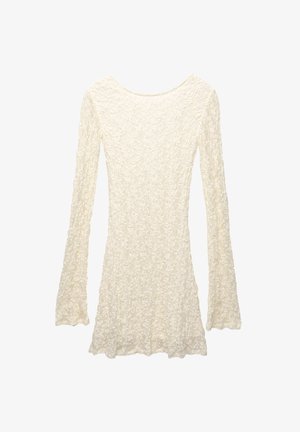 Lange mouw jurk in lichtcrème met een textuur en een bloemmotief. Heeft een ronde halslijn en zwierige mouwen die boven de taille eindigen.