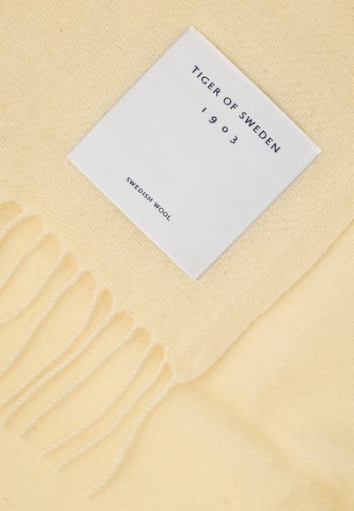 Žlutá švédská vlněná deka s třásněmi, na které je bílá nálepka s nápisem "TIGER OF SWEDEN 1903" a "SWEDISH WOOL".