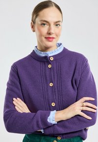 Cardigan viola con scollo rotondo e texture a coste, con chiusura a bottoni e una camicia blu a colletto sovrapposta.