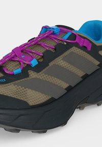 Chaussure de randonnée avec tige en mesh marron, bandes noires et grises, système de laçage rapide violet, œillets bleus et doublure intérieure rembourrée bleue.