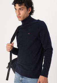 Marineblauer Rollkragenpullover aus weichem Strickstoff, mit einem kleinen Logodetail auf der Brust sowie gerippten Bündchen und Saum. Lässiger Schnitt.
