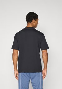 T-shirt noir à manches courtes avec un col rond, fabriqué en coton doux. Présente une coupe décontractée et une texture lisse. Vue de dos montrée.