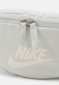 Nike tillbehörsväska i ljusgrått tyg, med en slät yta, dubbel dragkedja och en stor, präglad logotyp i en matchande nyans.