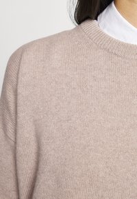 Jasnoróżowy sweter z prążkowanym okrągłym dekoltem i miękką teksturą dzianiny. Projekt zawiera lekko opadające ramiona.