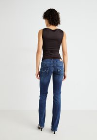 Top negro ajustado sin mangas y jeans de campana azul oscuro con sutiles arrugas y dos bolsillos traseros. Textura suave, corte entallado, detalles mínimos.