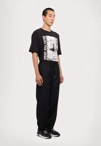 Black graphic t-shirt featuring a print and text on front, paired with loose black pants. The outfit is completed with black sneakers.