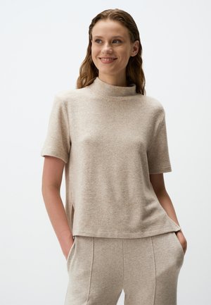 Top beige a maniche corte con collo alto, realizzato in un materiale morbido e testurizzato. Presenta spacchi laterali e una vestibilità rilassata.