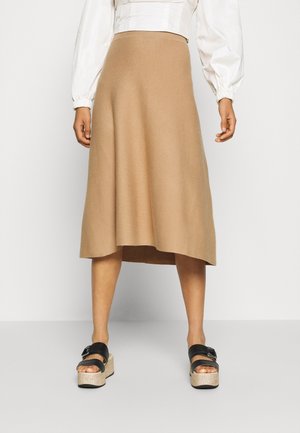 Strikket midi-nederdel i beige med en udvidet form og minimalistisk design. Kombineret med sorte platformssandaler for kontrast.