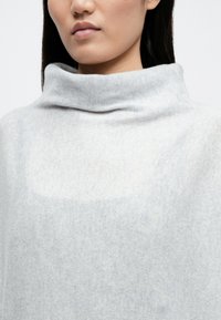 Ανοιχτό γκρι πουλόβερ πλεκτού με ψηλό, διπλωμένο λαιμό. Το ύφασμα φαίνεται μαλακό και υφή, με μία διακριτική λεπτομέρεια σε όλη την επιφάνεια.
