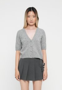 Cardigan gris à manches courtes avec un col en V, orn�é d'accents en perles et de boutons sur le devant, associé à une jupe plissée gris foncé.