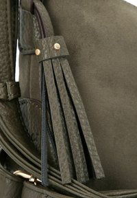 Grüne Ledertasche mit strukturierten Oberflächen, mehreren Quasten und goldenen Hardware-Akzenten, die eine Mischung aus glatten und Wildleder-Oberflächen hervorhebt.