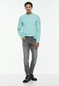 Mintgrön långärmad henleytröja med tre knappar, kombinerad med smala grå jeans och svarta snörkängor. Minimalistisk design.