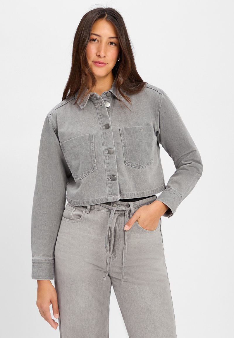 Przycięta szara kurtka dżinsowa z dwiema przednimi kieszeniami i guzikami, w połączeniu z pasującymi szarymi spodniami z wiązaniem w talii oraz detalem kieszeni.