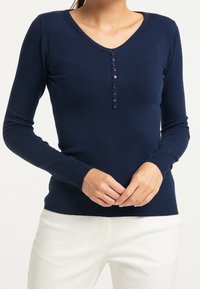 Marinblå långärmad tröja med V-ringning, med knapplist och ribbade ärmslut och nederkant. Mjuk tygtextur.