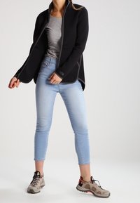 Giacca nera con dettagli grigi, maglietta grigia, jeans attillati azzurro chiaro e scarpe da esterno grigio-marrone con dettagli neri e rossi.