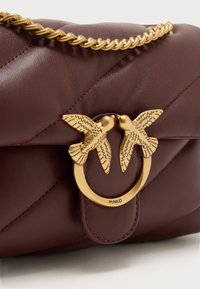 Χειροποίητη δερμάτινη τσάντα ώμου σε μπορντό χρώμα με καπιτονέ σχέδιο, χρυσή αλυσίδα και χρυσό κούμπωμα σε σχήμα δαχτυλιδιού με δύο πουλιά που φιλιούνται.