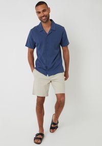 Marine kantoenshirt met korte mouwen, beige shorts en zwarte sandalen. Glad materiaal, comfortabele pasvorm en zichtbare knoopdetails.